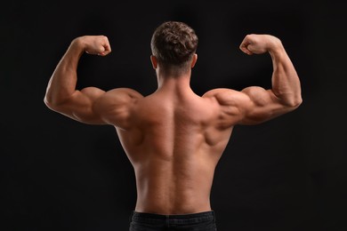 Photo of Muscular man showing his strength on black background, back view. Sexy body