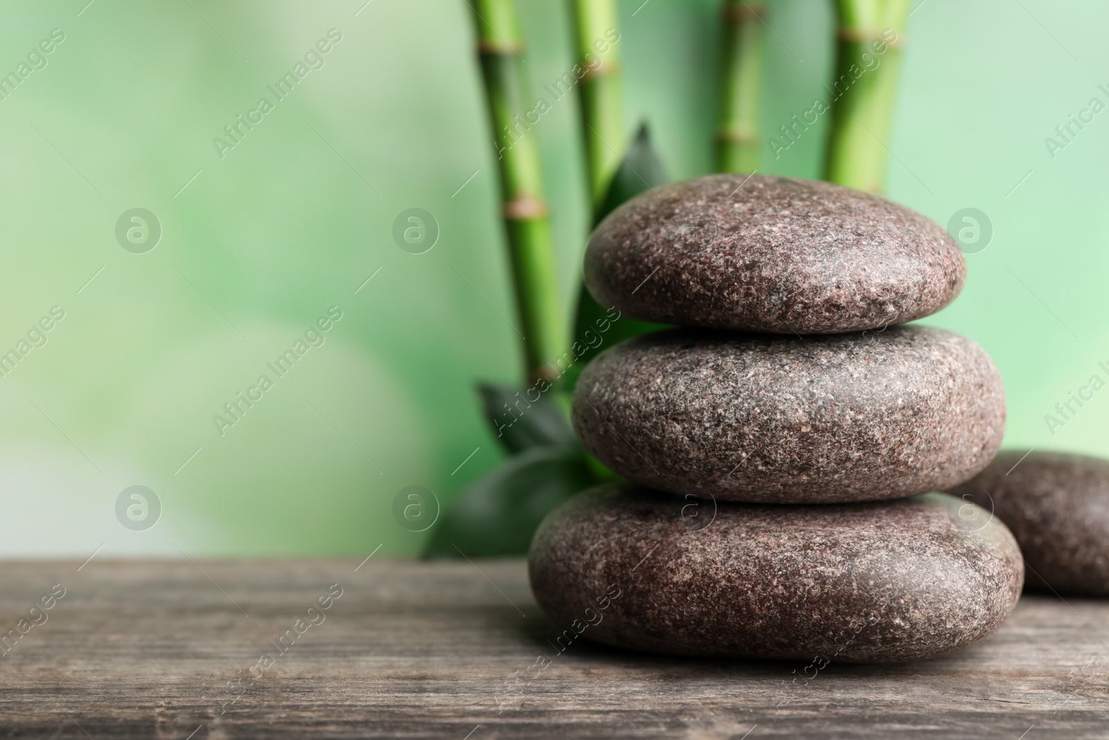 Photo of Stacked spa stones on wooden table against bamboo stems and green leaves. Space for text