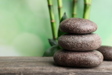 Photo of Stacked spa stones on wooden table against bamboo stems and green leaves. Space for text