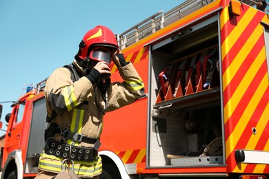 Firefighter in uniform wearing helmet and mask near fire truck outdoors, low angle view