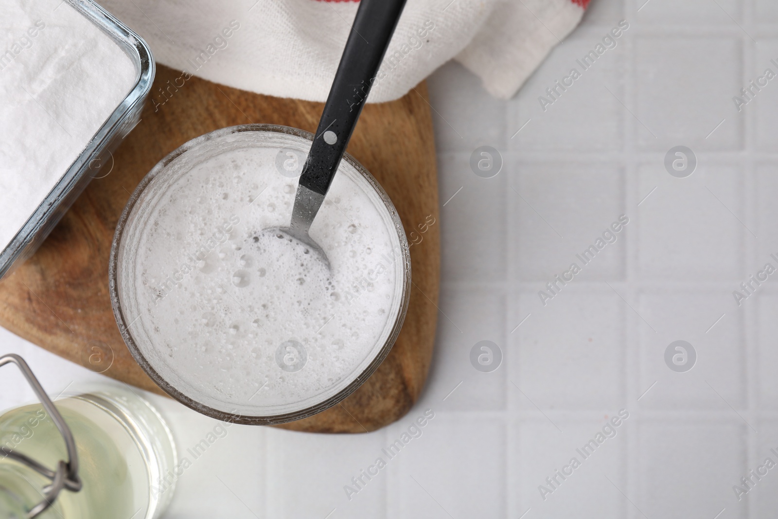 Photo of Chemical reaction of vinegar and baking soda in glass bowl on white tiled table, top view. Space for text