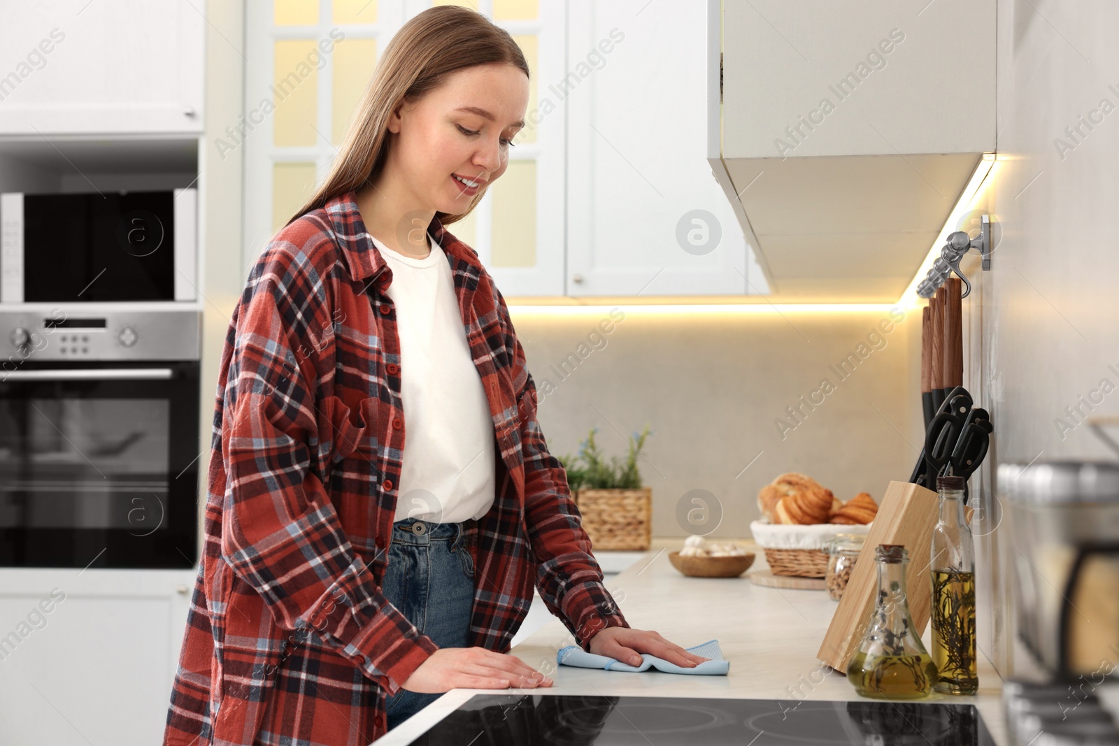 Photo of Woman with microfiber cloth cleaning white marble countertop in kitchen