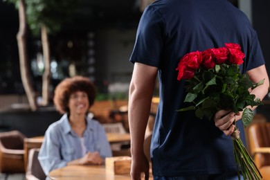 Photo of International dating. Man hiding bouquet of roses for his beloved woman in restaurant, closeup