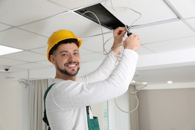 Electrician with pliers repairing ceiling wiring indoors