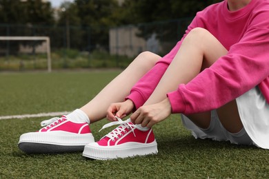 Photo of Woman tying shoelace of classic old school sneaker on green court outdoors, closeup
