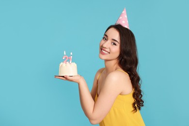 Photo of Coming of age party - 21st birthday. Smiling woman holding delicious cake with number shaped candles on light blue background