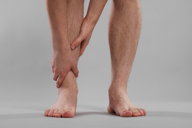 Man suffering from leg pain on grey background, closeup