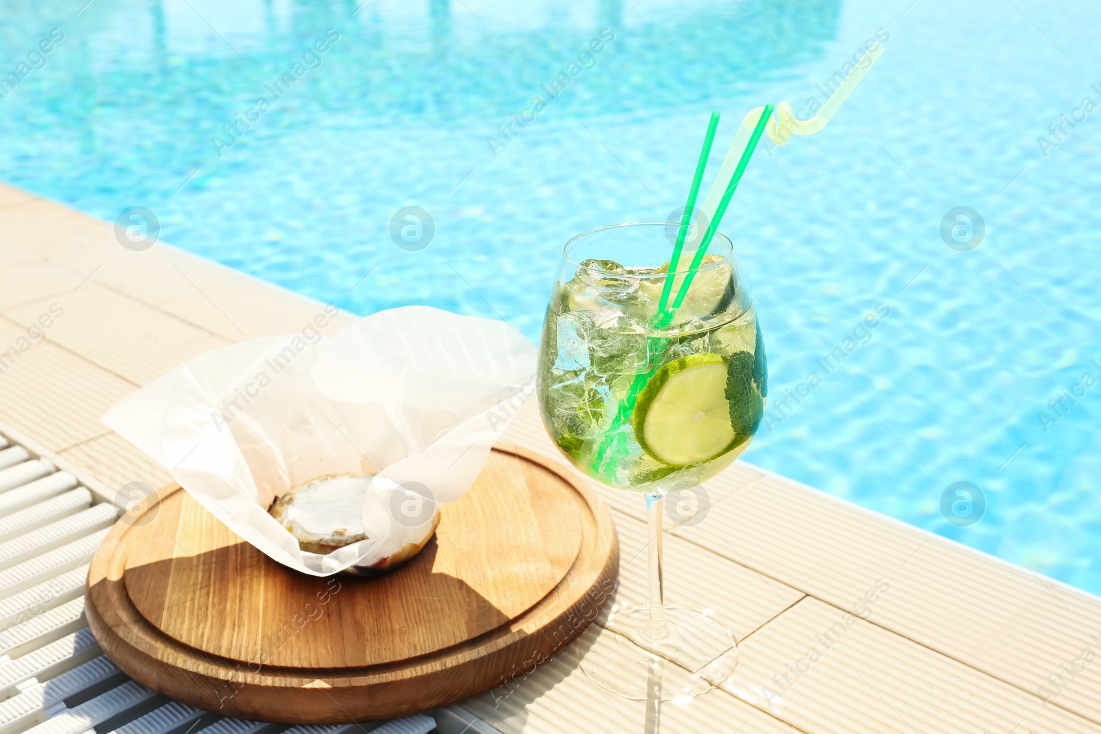 Photo of Glass of delicious mojito and brie cheese near swimming pool. Refreshing drink