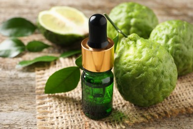 Photo of Bottle of essential oil and fresh bergamot fruits on wooden table, closeup