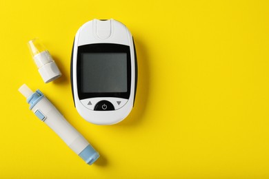 Digital glucometer and lancet pen on yellow background, flat lay with space for text. Diabetes control