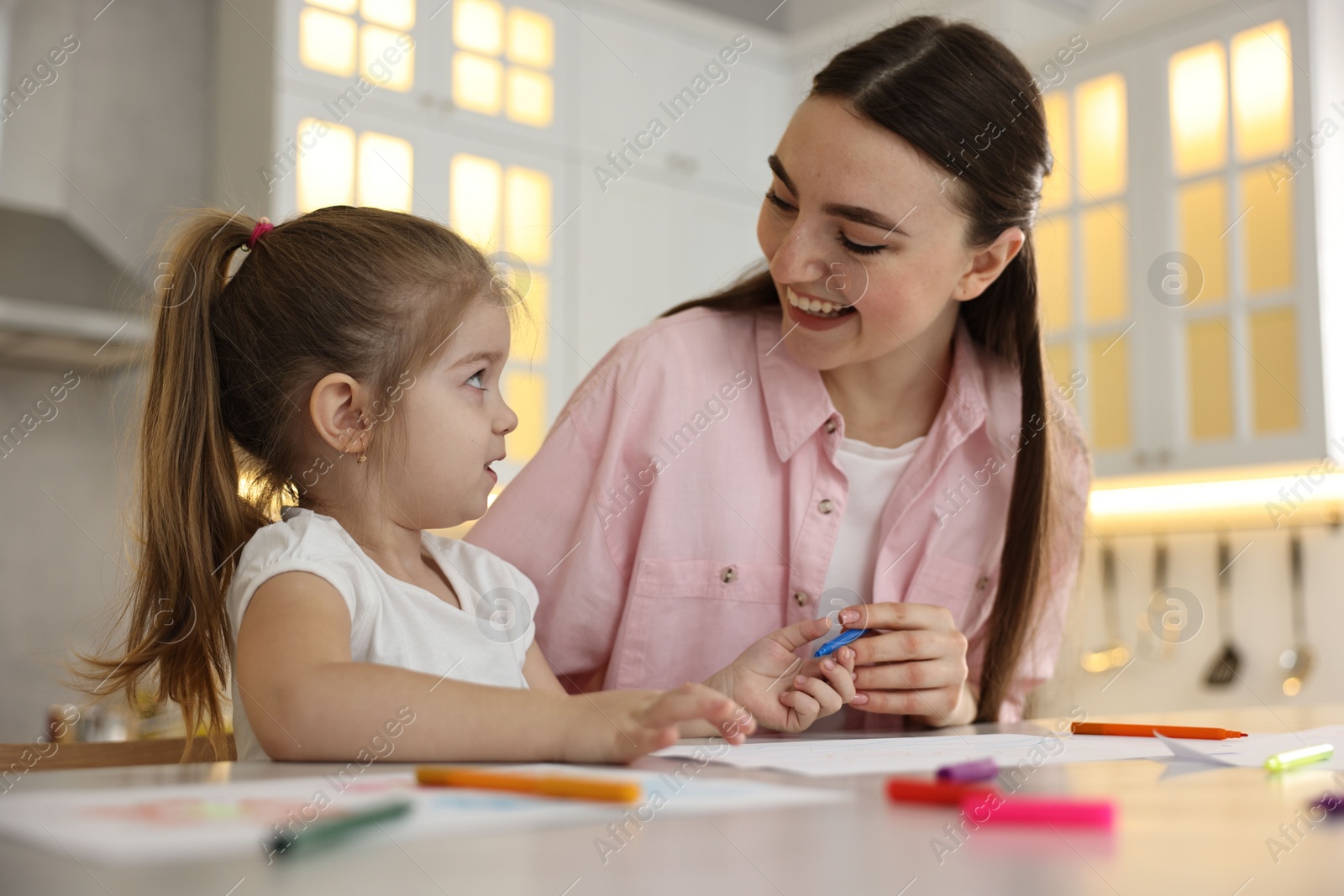 Photo of Mother and her little daughter drawing with colorful markers at table in kitchen