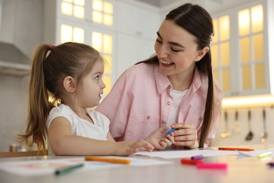 Photo of Mother and her little daughter drawing with colorful markers at table in kitchen