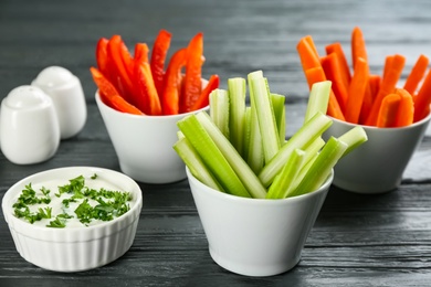 Celery and other vegetable sticks in bowls with dip sauce on grey wooden table