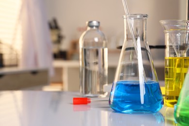 Laboratory analysis. Glassware with different liquids on white table indoors, closeup. Space for text