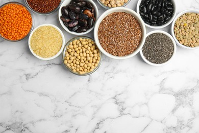 Different grains, seeds and space for text on white marble table, flat lay. Veggie diet