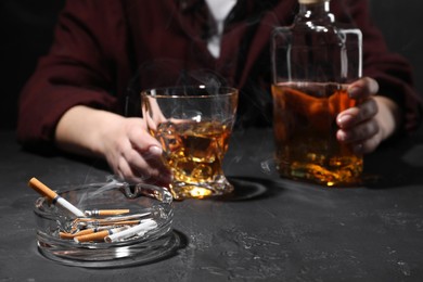 Alcohol addiction. Woman with whiskey and smoldering cigarettes at dark textured table, selective focus