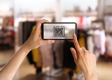 Image of Woman holding smartphone with QR code on screen in store, closeup