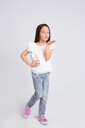 Cute little girl blowing air kiss on light grey background