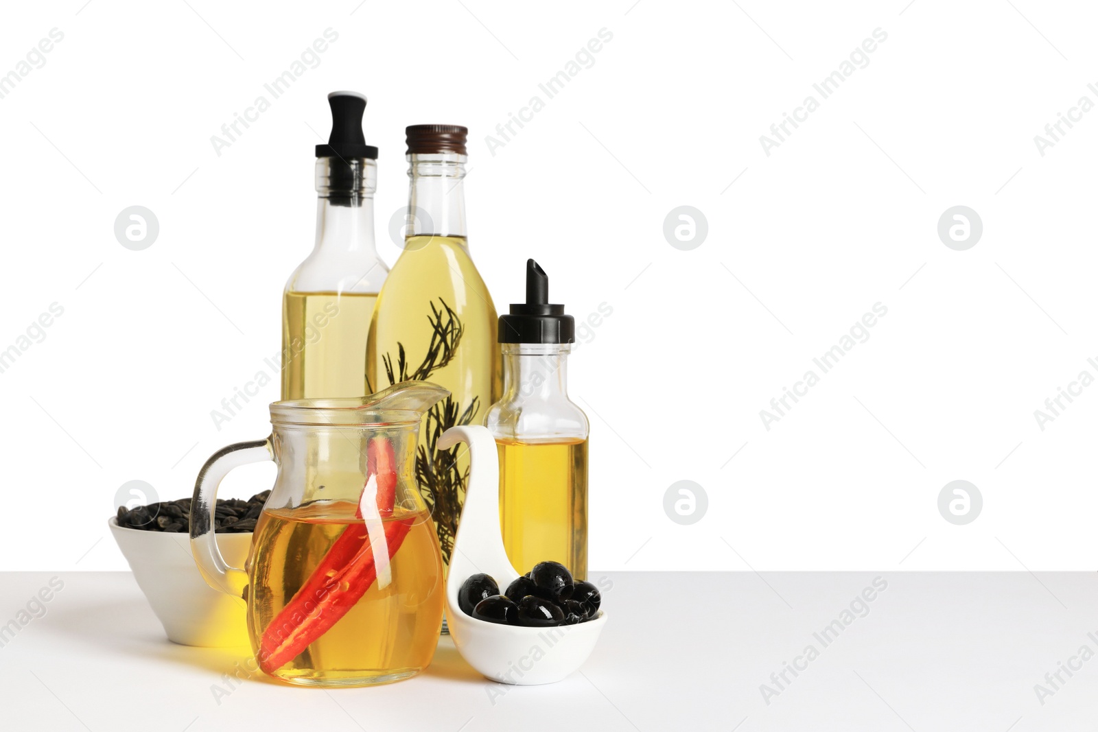 Photo of Bottles of different cooking oils, olives and sunflower seeds on white background, space for text