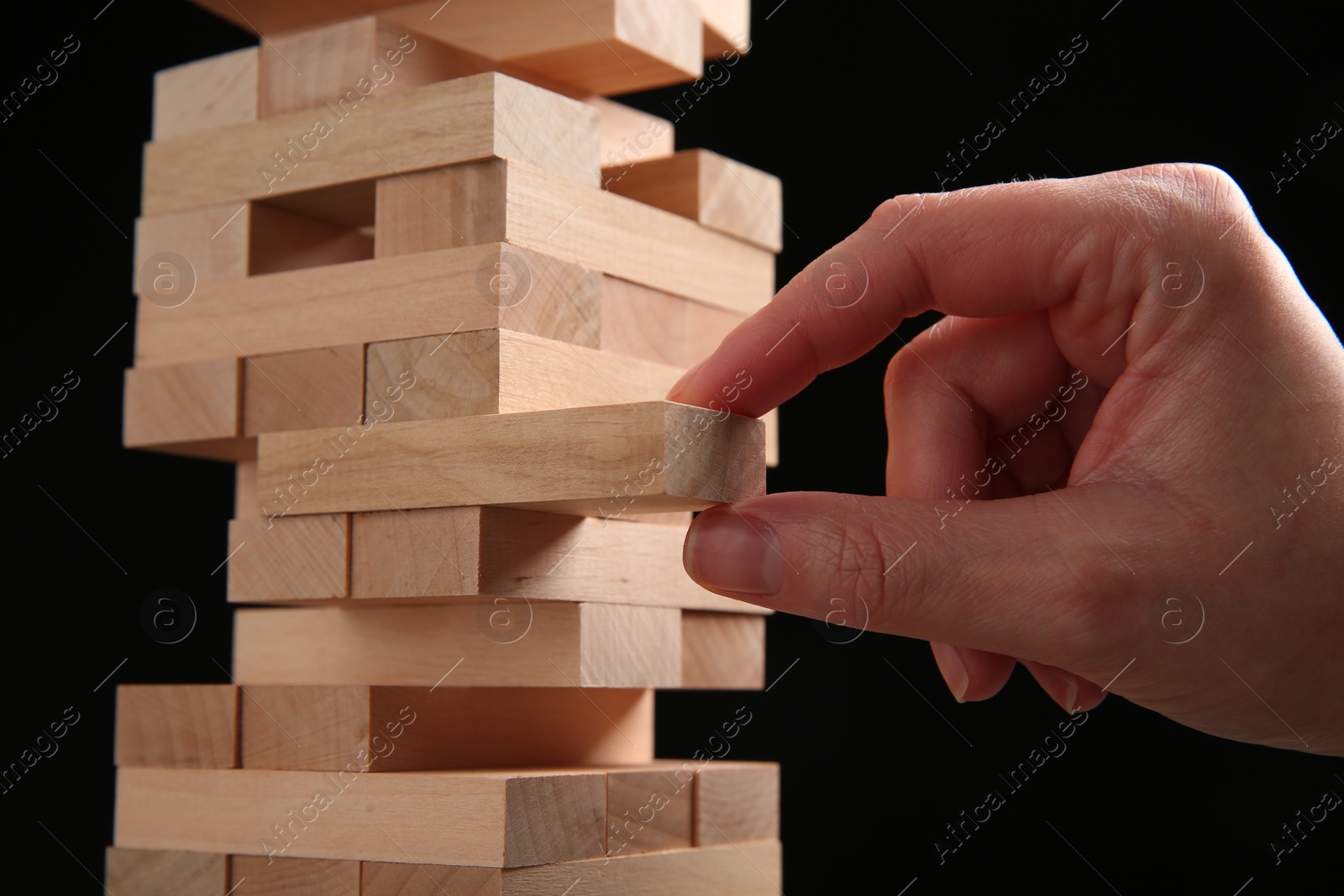 Photo of Woman playing Jenga on black background, closeup