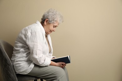 Photo of Elderly woman with poor posture reading book on beige background. Space for text