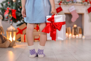 Photo of Cute little child in warm socks with Christmas gift box at home