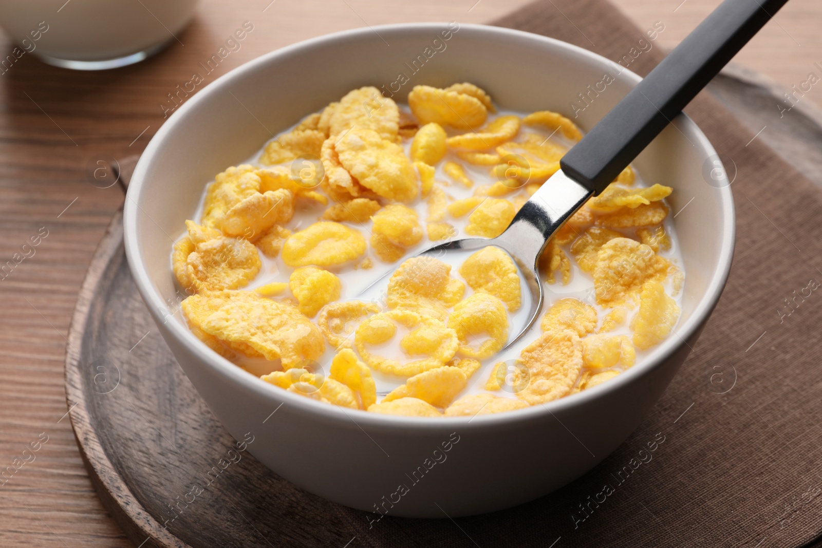 Photo of Spoon with tasty cornflakes and milk in bowl on wooden table, closeup