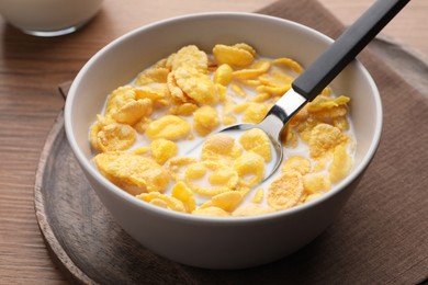 Photo of Spoon with tasty cornflakes and milk in bowl on wooden table, closeup