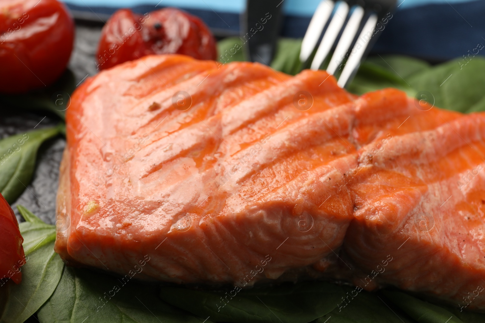 Photo of Tasty grilled salmon with tomatoes and spinach on plate, closeup