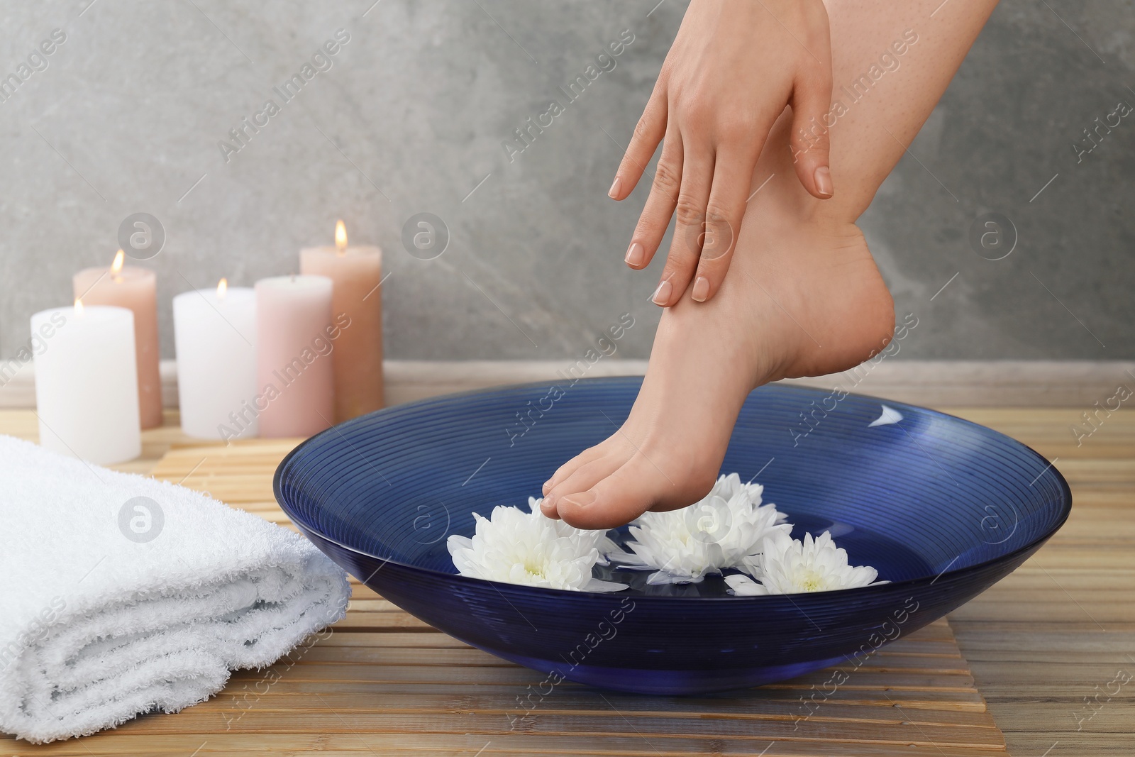 Photo of Woman soaking her feet in bowl with water and flowers on floor, closeup. Spa treatment