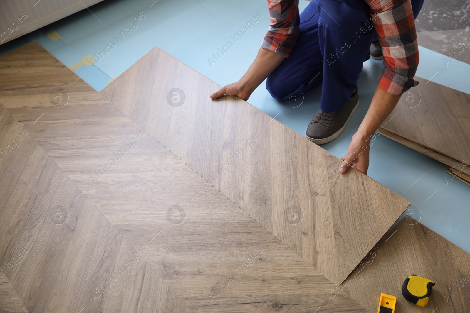 Photo of Worker installing laminated wooden floor indoors, closeup