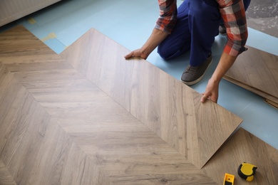 Worker installing laminated wooden floor indoors, closeup