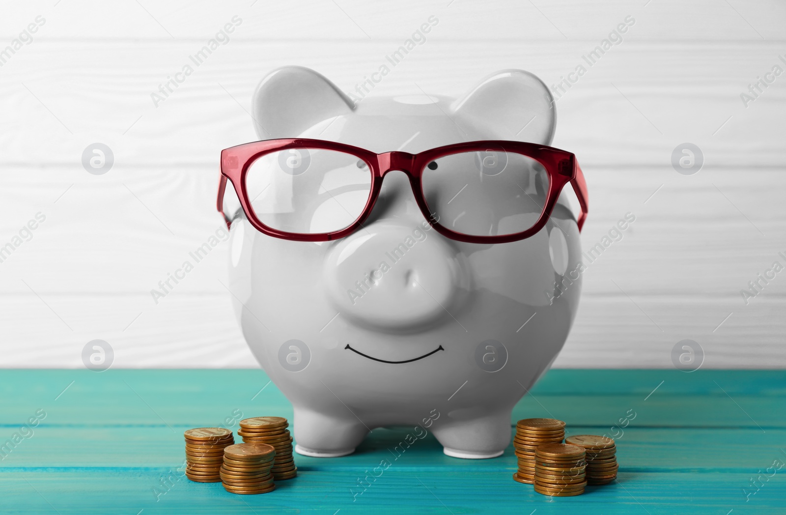 Photo of Ceramic piggy bank with glasses and coins on turquoise wooden table