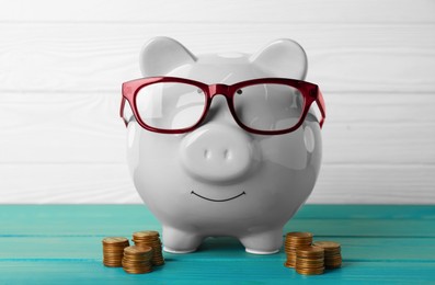 Ceramic piggy bank with glasses and coins on turquoise wooden table