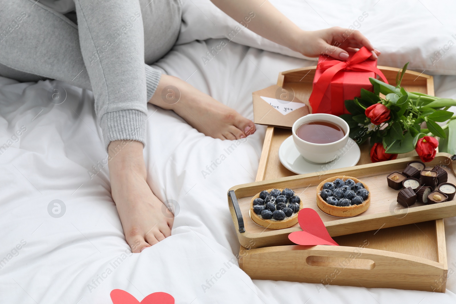 Photo of Tasty breakfast served in bed. Woman with gift box, tea, desserts and flowers at home, closeup