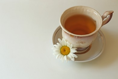 Photo of Tasty herbal tea and fresh chamomile flower on white table, space for text