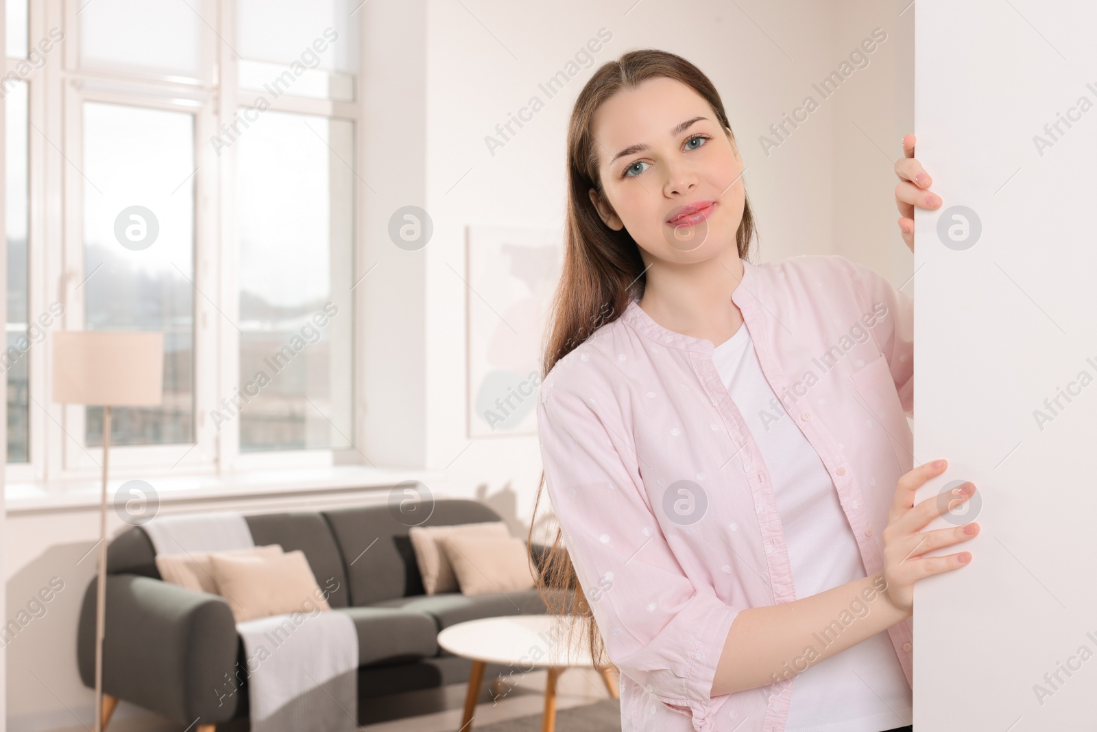 Photo of Beautiful woman standing near white wall at home. Invitation to come in room