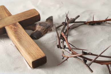 Crown of thorns, wooden cross and hammer on sand. Easter attributes