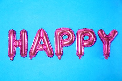 Word HAPPY made of pink foil balloon letters on light blue background