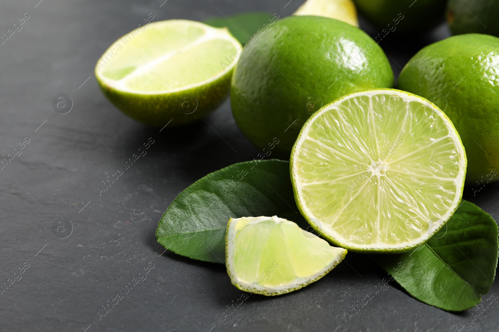 Photo of Fresh ripe limes and leaves on black table, closeup. Space for text