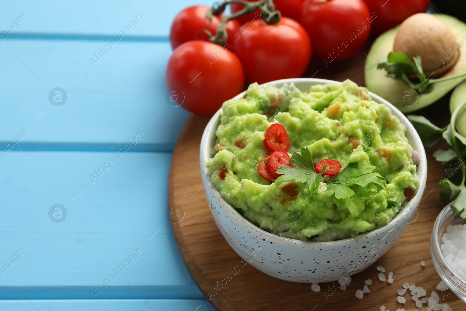 Photo of Delicious guacamole and ingredients on light blue wooden table, space for text