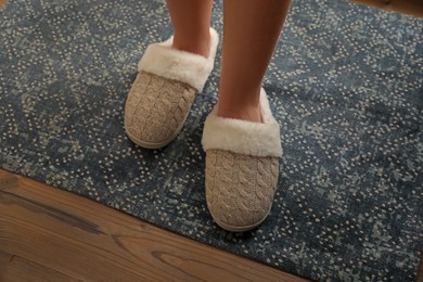 Photo of Woman wearing warm beige slippers on rug, closeup