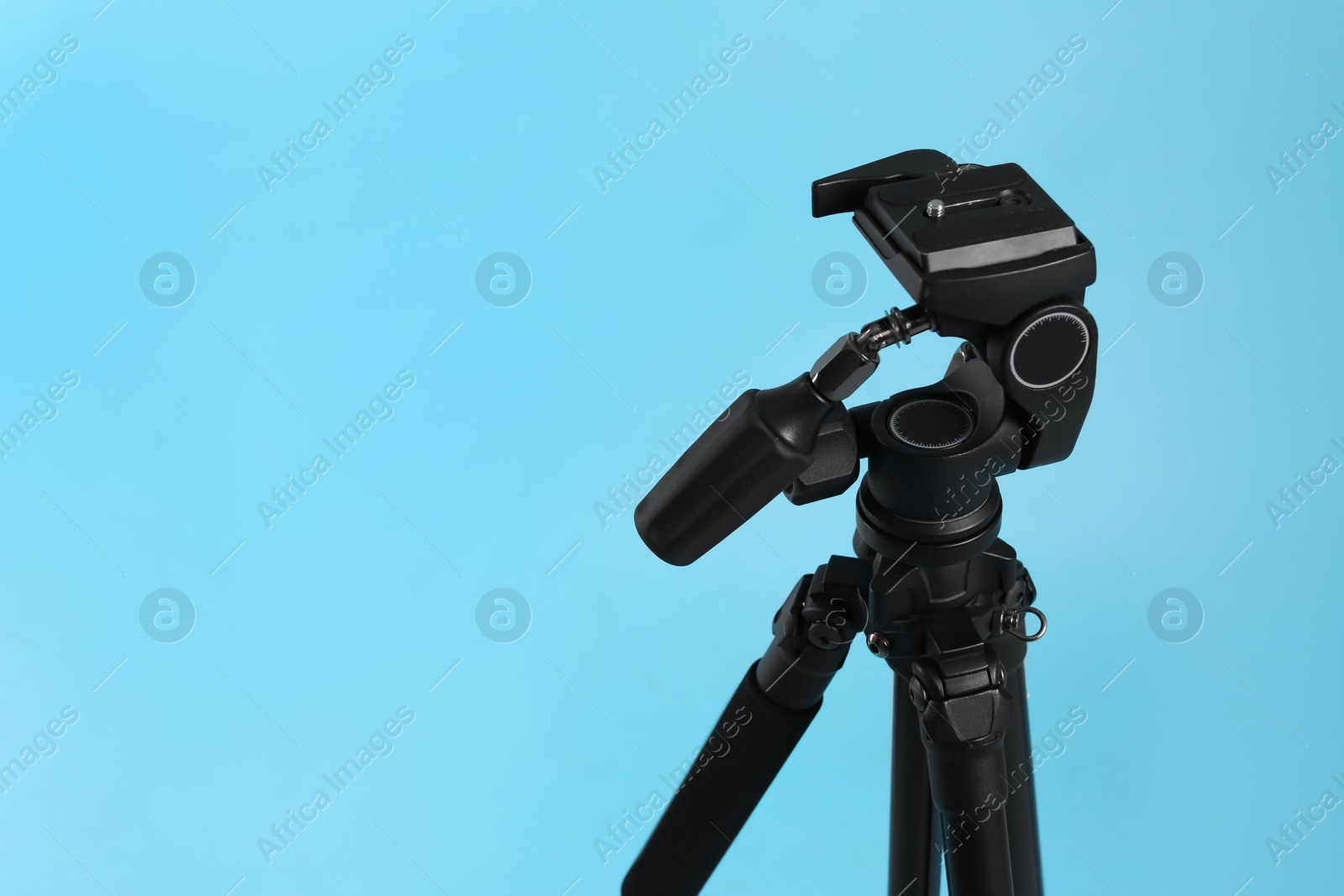 Photo of Modern tripod on light blue background. Space for text