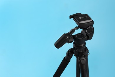 Modern tripod on light blue background. Space for text