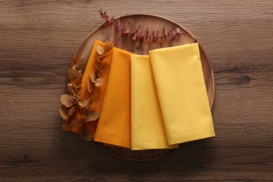 Tray with different kitchen napkins and decorative dry leaves on wooden table, top view