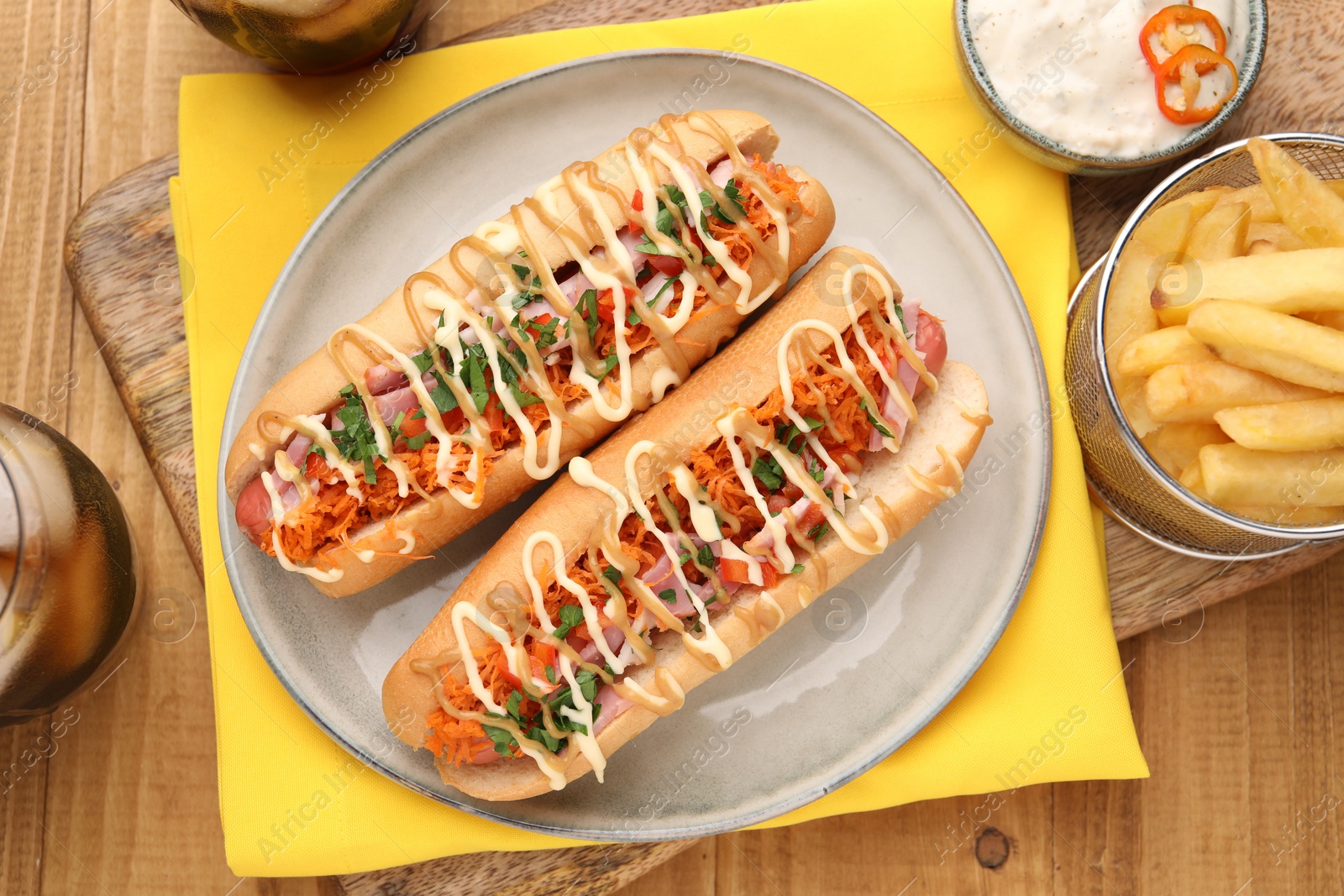 Photo of Delicious hot dogs with bacon, carrot and parsley served on wooden table, flat lay