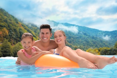 Image of Happy family in outdoor swimming pool at luxury resort with beautiful view of mountains on sunny day