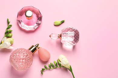 Photo of Flat lay composition with perfume bottles and flowers on light pink background, space for text
