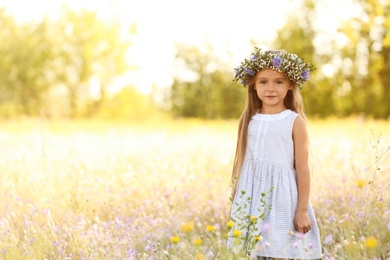 Photo of Cute little girl wearing flower wreath outdoors, space for text. Child spending time in nature