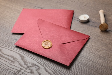 Photo of Envelopes with wax seal, candle and stamp on wooden table